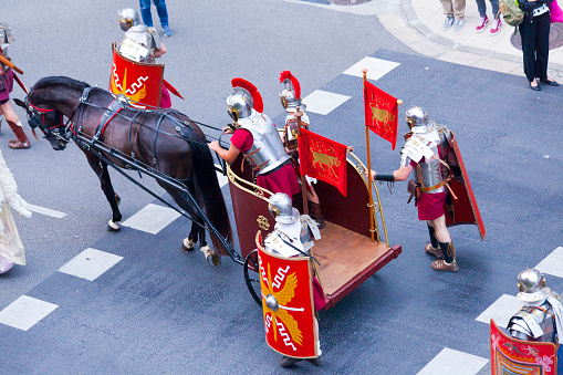 Lugo, Spain- June 11, 2022: Roman soldiers walking  with horse chariot , traditional festival recreation , high angle view of Arde Lucus traditional festival parade, Roman Historical Reenactment. Metal suit of armor, shield and helmet,. Lugo city, Galicia, Spain.
