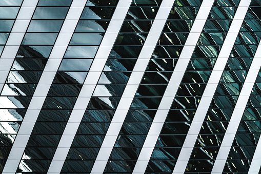 Modern building facade of glass and concrete reflecting outside buildings and environment. Complex architectural pattern close-up