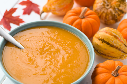 A bowl of pumpkin soup surrounded by mini pumpkins and gourds