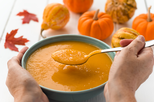 Woman's hands holding bowl and spoon with pumpkin soup