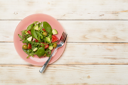 Fresh salad with arugula, spinach and vegetables on wooden background, top view.