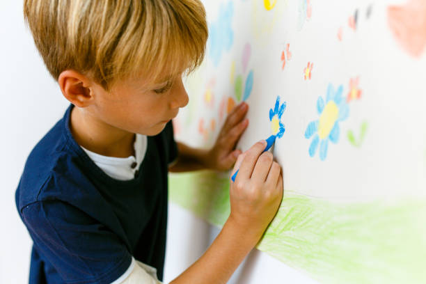 istock Little boy drawing with crayons on a paper roll sticked on the wall 1496997658