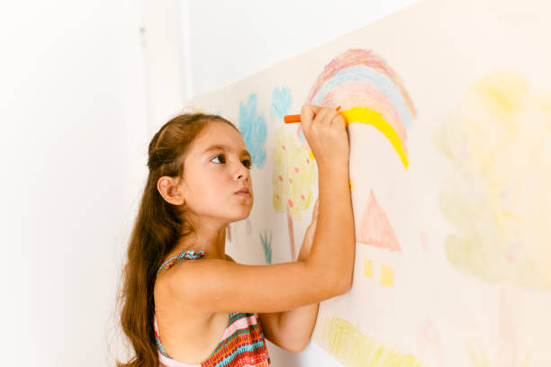 istock Little girl drawing with crayons on a paper roll sticked on a wall 1496997753