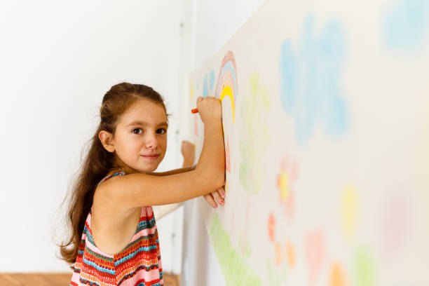 istock Little girl drawing with crayons on a paper roll sticked on a wall 1496997781