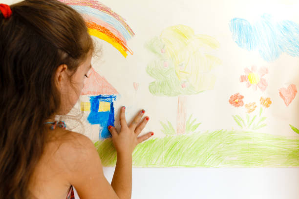 istock Little girl drawing with crayons on a paper roll sticked on a wall 1496997794
