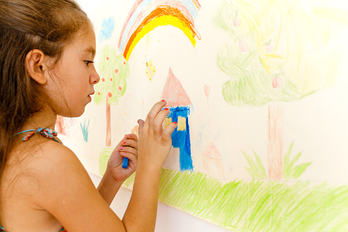 Little girl drawing with crayons on a paper roll sticked on a wall