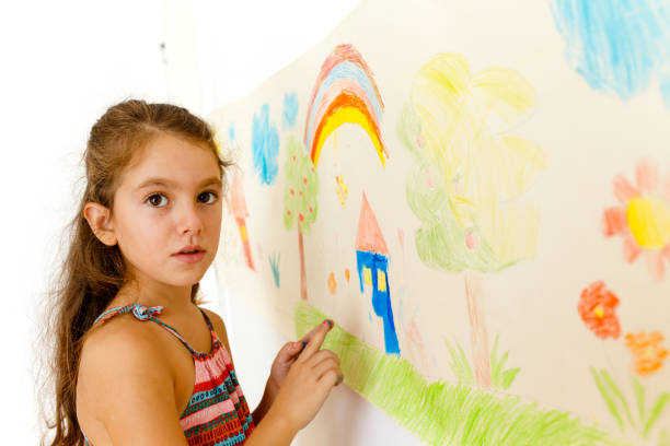 istock Little girl drawing with crayons on a paper roll sticked on a wall 1496997846