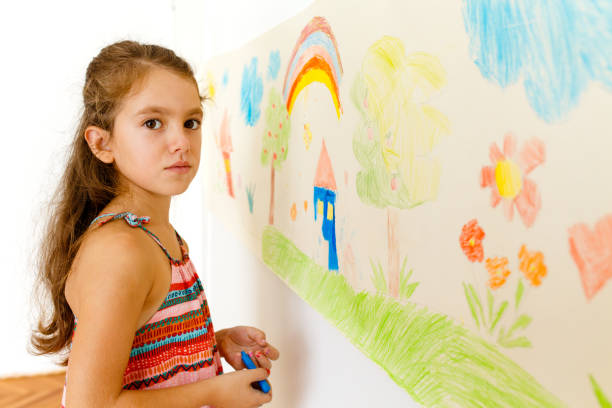 istock Little girl drawing with crayons on a paper roll sticked on a wall 1496997875