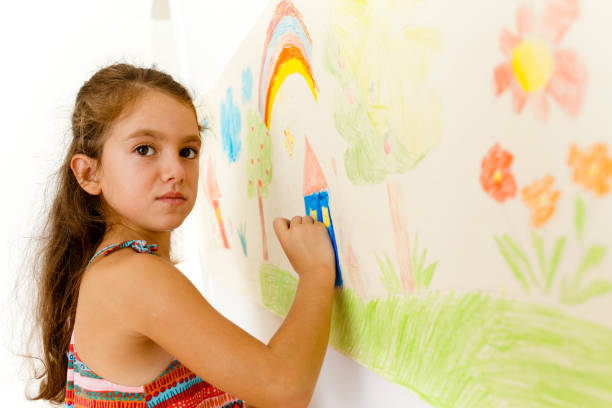 istock Little girl drawing with crayons on a paper roll sticked on a wall 1496997930