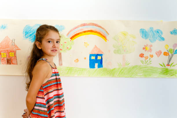 istock Little girl drawing with crayons on a paper roll sticked on a wall 1496997949