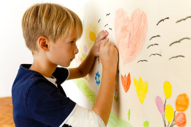 istock Little boy drawing with crayons on a paper roll sticked on the wall 1496998093
