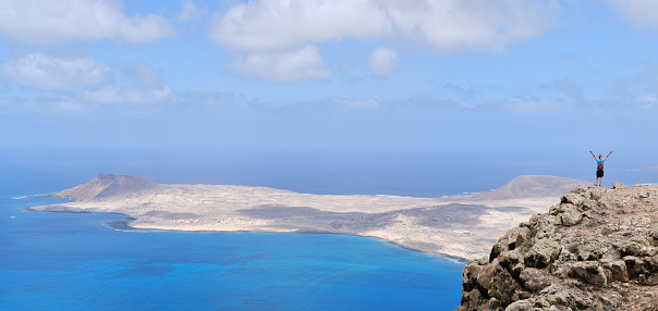Woman with arms raised on top of a hill. With La Graciosa Island in the background. Panoramic