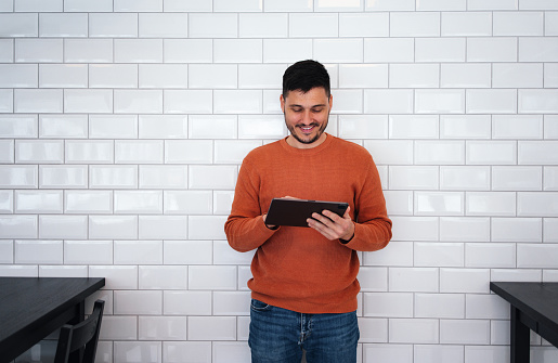 Happy man standing in front of white tiles wall and reading business report on his tablet.