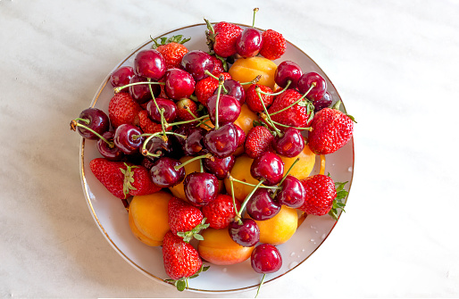 Fresh fruits of red cherries, strawberries, strawberries, peaches on a plate on a light background close-up. Top view