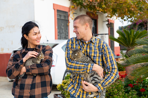 Caucasian man and Asian woman with two kitties standing outdoors.