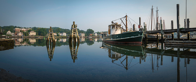 Mystic River summer landscape in Connecticut with moored trawler, commercial dock, piers, and water reflections