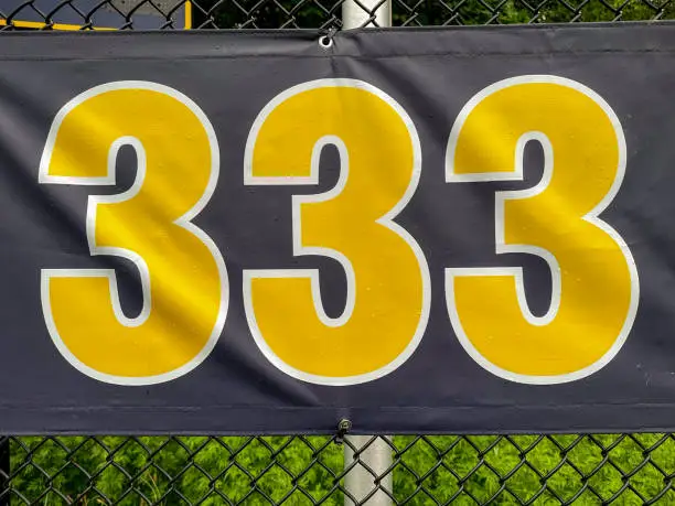 Photo of 333 foot ft baseball field distance sign in yellow and black mounted on the black vinyl outfield fence.