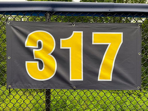 317 foot ft baseball field distance sign in yellow and black mounted on the black vinyl outfield fence.