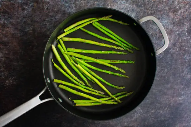 Sauteing thin asparagus spears in a large skillet frying pan