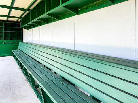 typical nondescript high school baseball, softball dugout with green bench and gray walls. No people visible. Not a ticketed event.