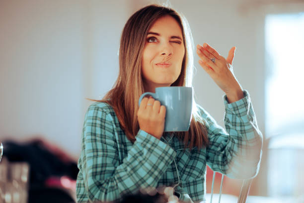 Woman Smelling Her Morning Beverage Feeling Repulse Person suffering from distorted smelling after long covid gross coffee stock pictures, royalty-free photos & images