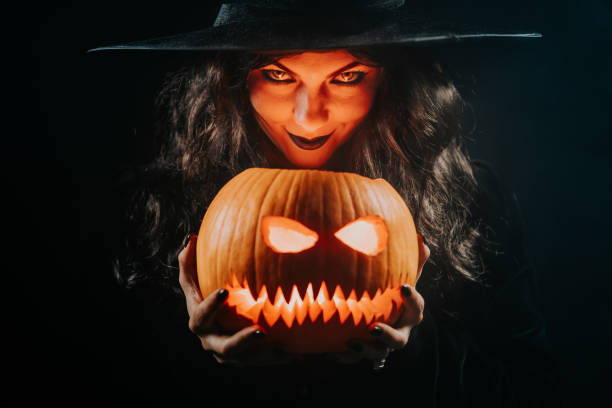 istock Mysterious black witch with pumpkin as head of jack-o-lantern on dark backdrop. Scary symbol of Halloween, masquerade costume, party decoration. Magic, classic hag 1497057925