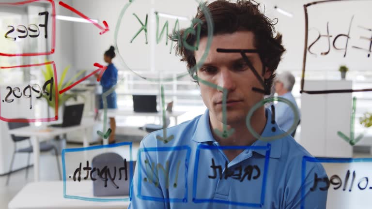 Young pensive man looking at data on glass board in modern office