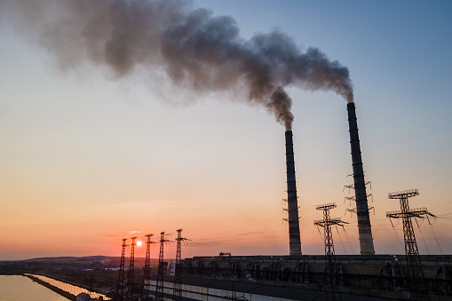 Aerial view of coal power plant high pipes with black smoke moving upwards polluting atmosphere at sunset. Production of electrical energy with fossil fuel concept.