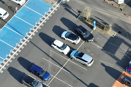 Aerial view of many colorful cars parked on parking lot with lines and markings for parking places and directions.