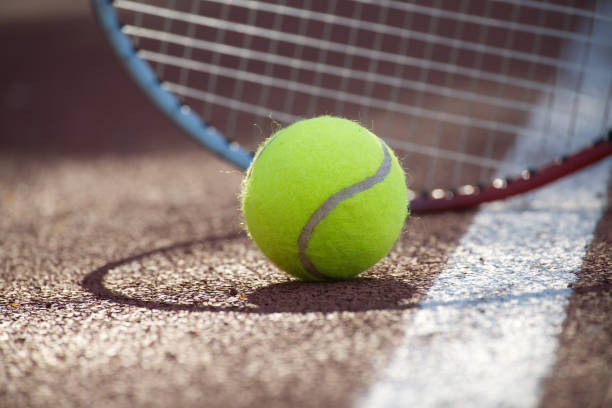 Tennis ball and racquet on outdoor court in sunshine stock photo