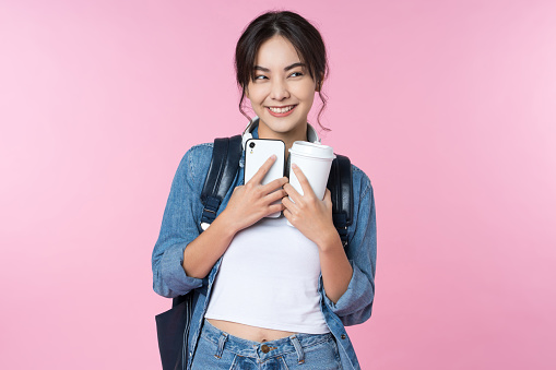 Portrait of young Asian woman student standing with smartphone coffee and backpack.College Teenager University concept.