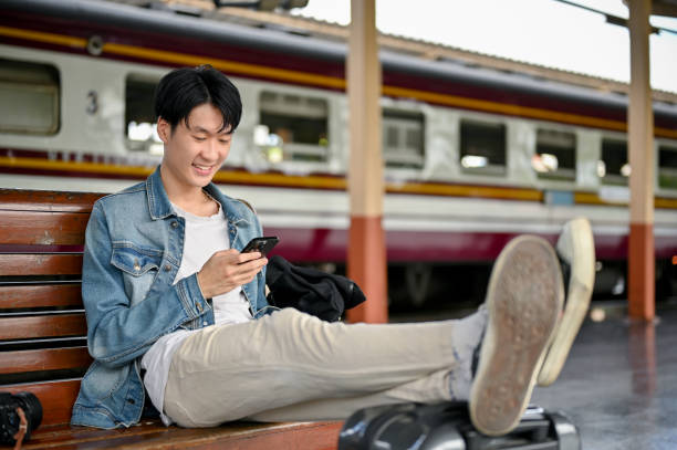 istock A happy Asian male backpacker using his smartphone on a bench while waiting for his train 1497076178
