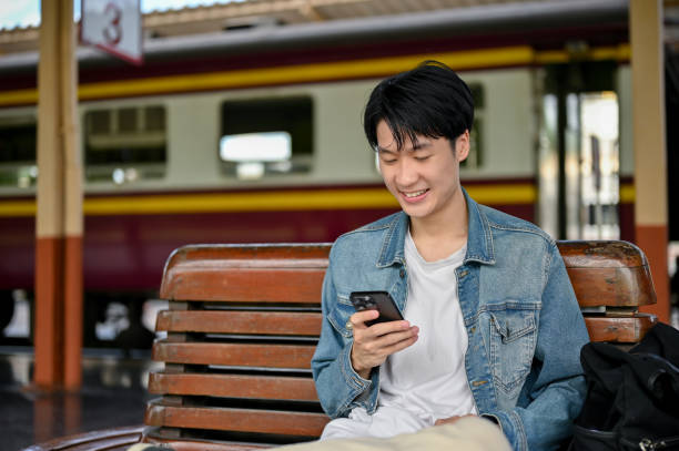 istock A happy Asian male backpacker using his smartphone while waiting for his train on a bench 1497076195