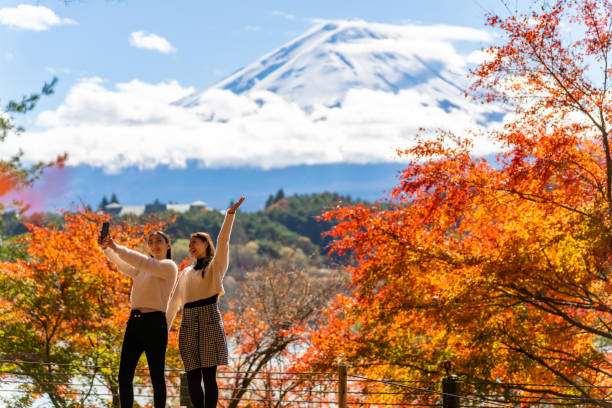 amigas asiáticas que usan un teléfono móvil para tomarse selfies juntas durante el viaje al monte fuji en otoño - prefectura de yamanashi fotografías e imágenes de stock