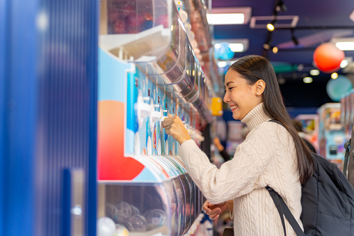 Happy Asian woman handle a doll from gashapon capsule toy vending machine while shopping in Tokyo city, Japan at night. Attractive girl enjoy and fun outdoor travel city street on autumn holiday vacation