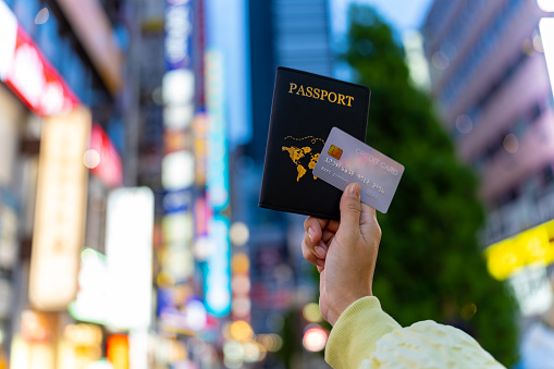 Asian woman hand holding passport and credit card with crowd of people walking and shopping at Shibuya, Tokyo city, Japan background. Global travel transportation, business banking and payment concept