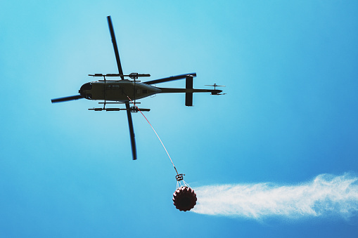 A helicopter flies back to a a forest fire with a bucket of water.