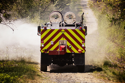 An off-road firetruck sprays the edge of a dirt road near a forest fire.