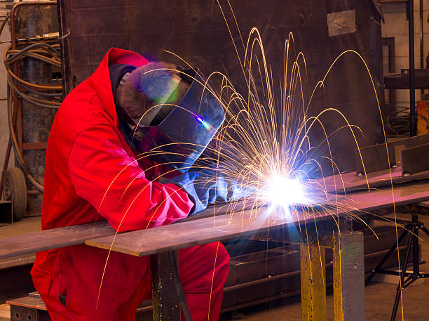 istock Welder bends to cut metal beam with orange sparks. 149708550