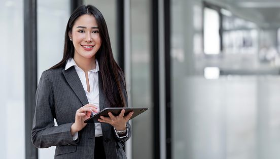 Young Asian businesswoman looking at camera holding  tablet at office.