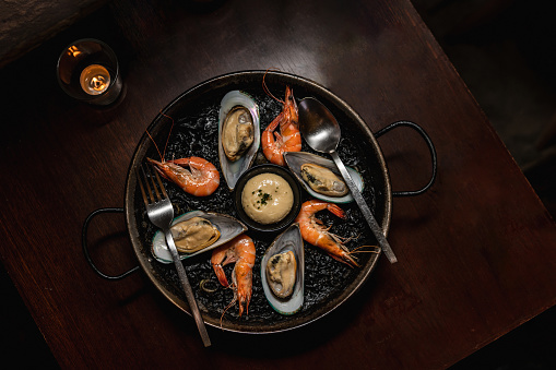 Delicious black risotto with shrimps and mussels on dinning wooden table, top view.