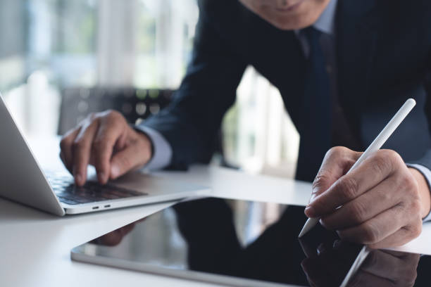 istock Businessman using digital tablet and working on laptop computer on office table. Corportae man using stylus pen proofing and signing business contract on tablet pc 1497095528