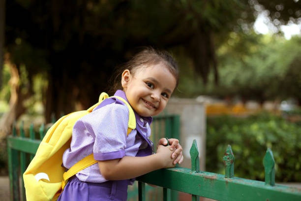 Small cute elementary age schoolgirl climbing on iron grill during day time.