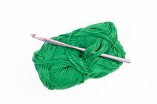 Dark green thread spool with purple crochet hook, isolated on white background.