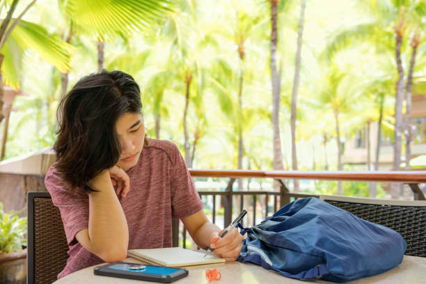 Giovane donna che scrive nel quaderno all'aperto in posizione tropicale - foto stock