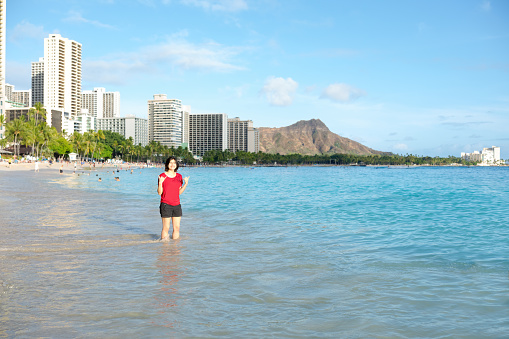 Young woman wading knee deep along Waikiki and Kuhio beach, Oahu, Hawai with Diamond Head crater in background