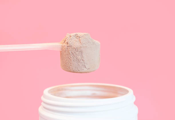 Chocolate protein powder in scoop and plastic jar on pink background.