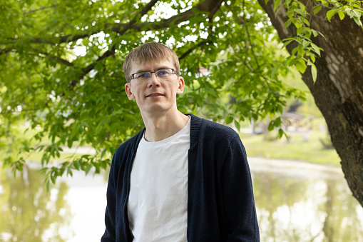 Portrait Of Tall Blond 40 Yo Man In Eyesight Glasses, Smiling Looking At Camera, Green Tree And Lake On Background. Horizontal Plane. High quality photo