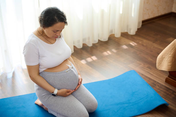 Overhead view pregnant woman holding her hands on belly, practicing relaxation exercises in homely tranquil atmosphere