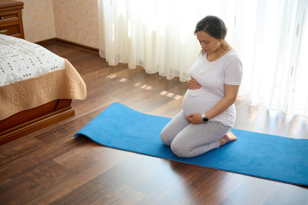 Pregnant woman expecting baby, holding her hands on belly, practicing relaxation exercises in homely tranquil atmosphere